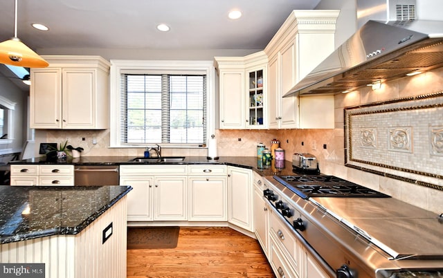 kitchen with appliances with stainless steel finishes, decorative light fixtures, sink, light hardwood / wood-style floors, and wall chimney range hood