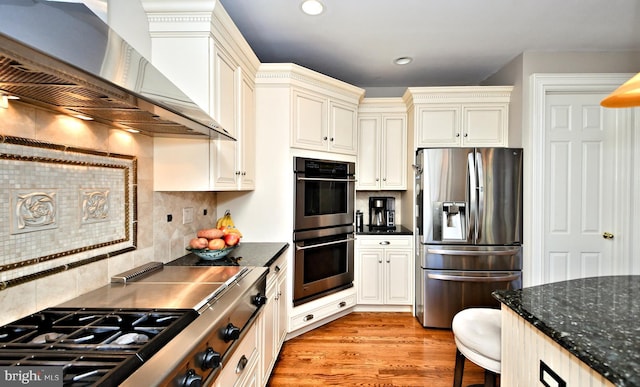 kitchen featuring appliances with stainless steel finishes, ventilation hood, a breakfast bar area, backsplash, and light wood-type flooring