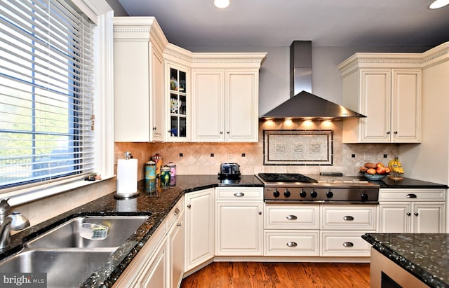 kitchen featuring sink, light hardwood / wood-style flooring, stainless steel gas cooktop, dark stone counters, and wall chimney exhaust hood