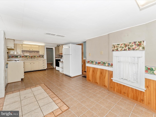 kitchen with white fridge, wood walls, cream cabinets, and stove