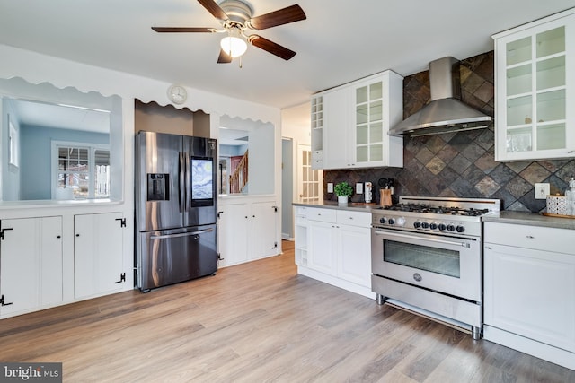 kitchen with stainless steel appliances, white cabinetry, wall chimney range hood, and light wood-type flooring