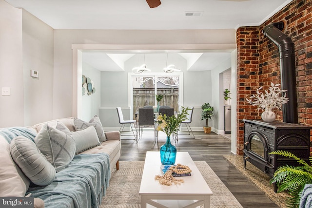 living room featuring ceiling fan, brick wall, dark hardwood / wood-style floors, and a wood stove