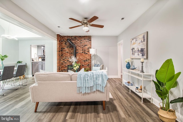 living room featuring sink, wood-type flooring, ceiling fan, and a wood stove