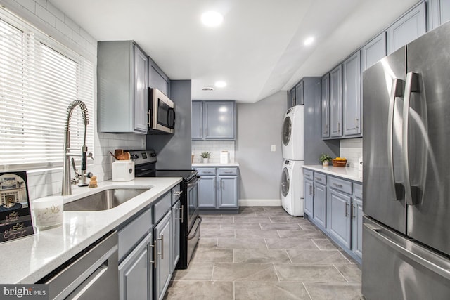 kitchen featuring sink, gray cabinetry, backsplash, stacked washer and clothes dryer, and stainless steel appliances