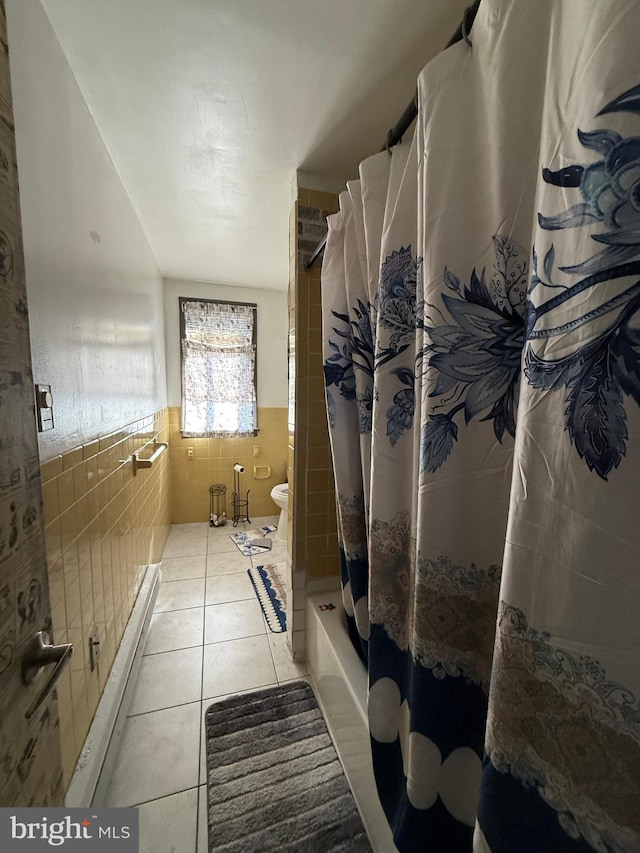 full bathroom with toilet, a wainscoted wall, shower / tub combo with curtain, tile patterned flooring, and tile walls