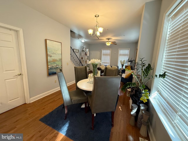 dining space featuring ceiling fan with notable chandelier, dark wood-style flooring, baseboards, and stairs