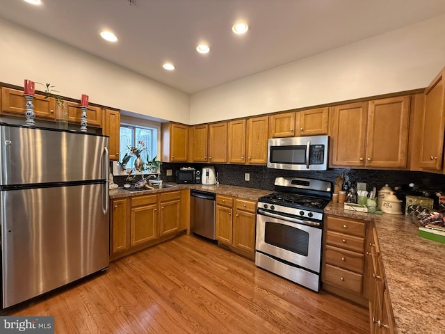 kitchen featuring brown cabinetry, backsplash, stainless steel appliances, and light wood-style floors