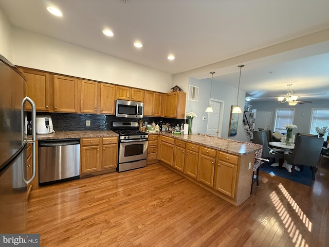 kitchen featuring a peninsula, brown cabinets, appliances with stainless steel finishes, and pendant lighting