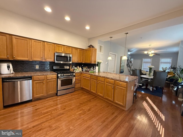 kitchen with stainless steel appliances, hanging light fixtures, brown cabinetry, open floor plan, and a peninsula