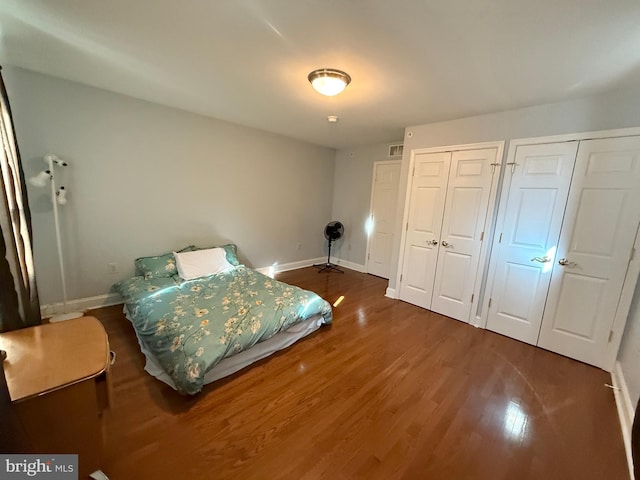 bedroom with visible vents, wood finished floors, two closets, and baseboards