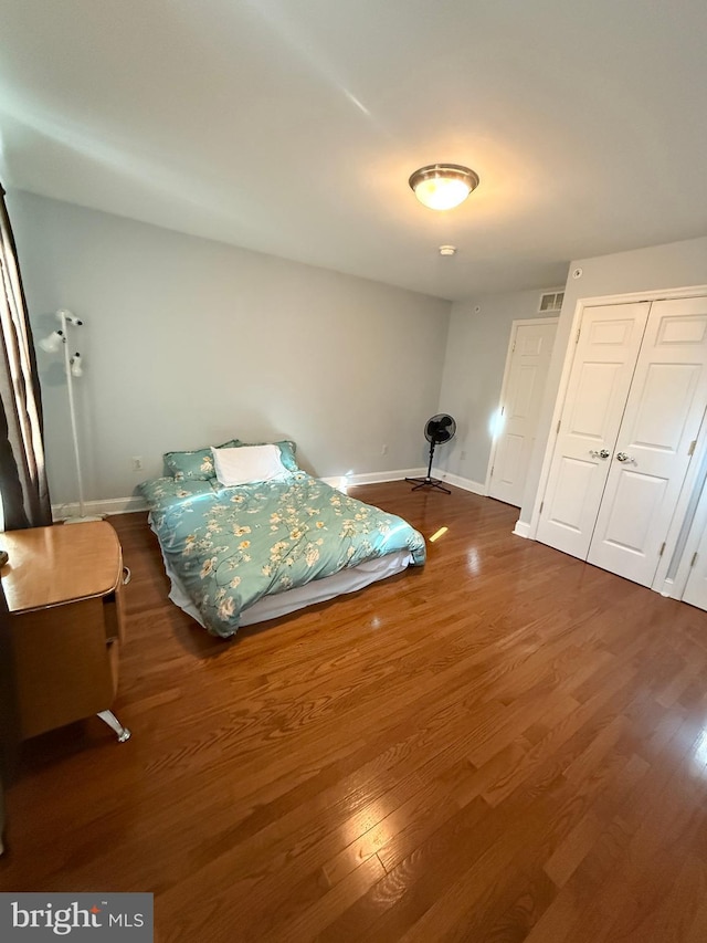 bedroom featuring visible vents, baseboards, dark wood finished floors, and a closet