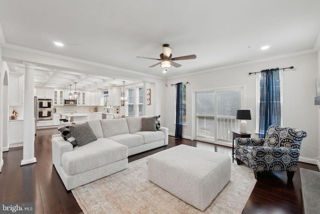 living room featuring decorative columns, wood-type flooring, ornamental molding, coffered ceiling, and ceiling fan