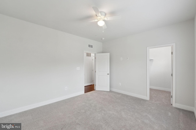 unfurnished bedroom featuring a spacious closet, light carpet, ceiling fan, and a closet