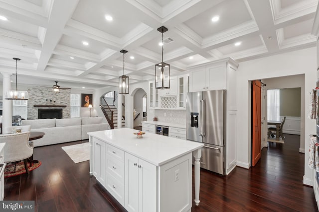 kitchen featuring a fireplace, high quality fridge, white cabinets, a kitchen island, and decorative light fixtures