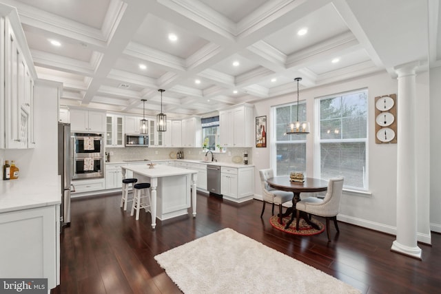 kitchen with white cabinetry, a kitchen island, stainless steel appliances, a kitchen bar, and decorative light fixtures