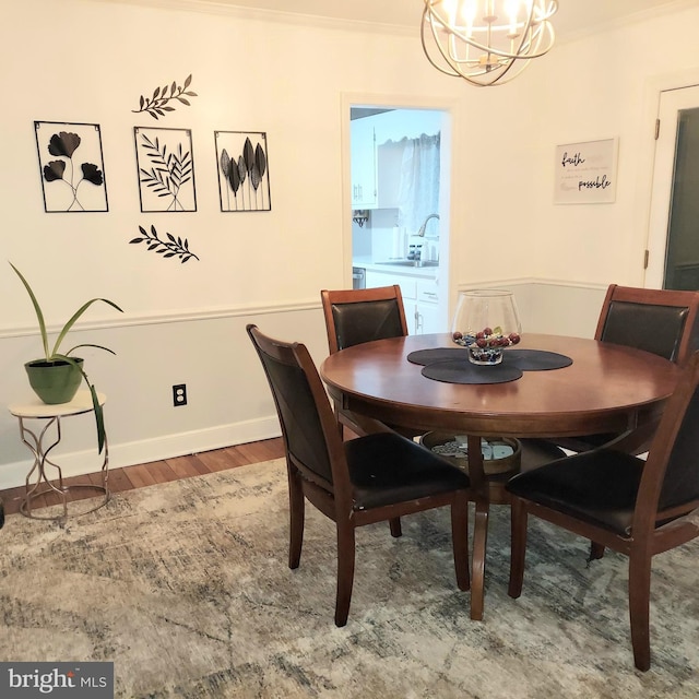 dining area with sink, wood-type flooring, ornamental molding, and a chandelier