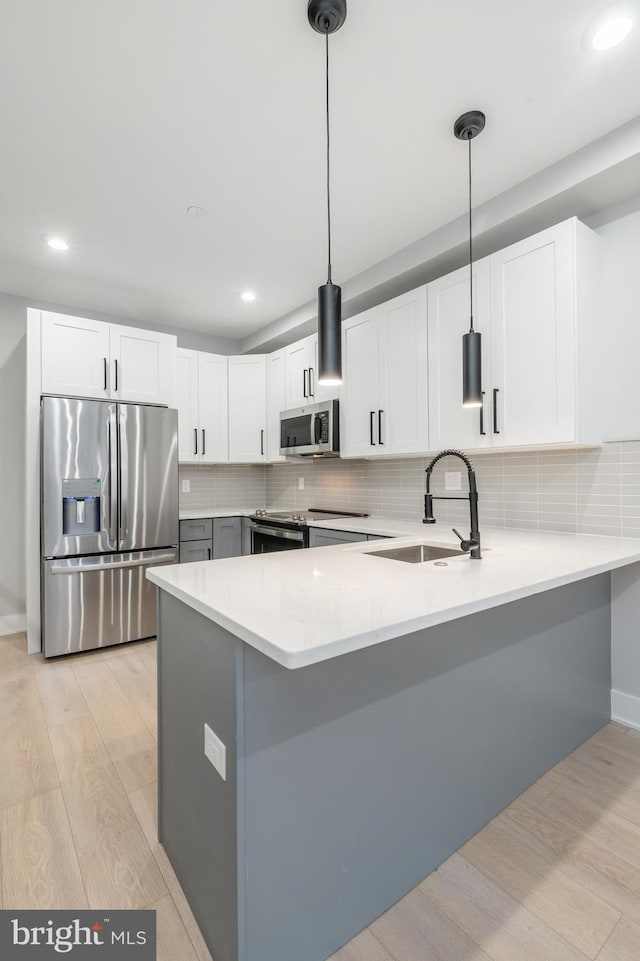 kitchen with a peninsula, stainless steel appliances, light countertops, light wood-type flooring, and a sink