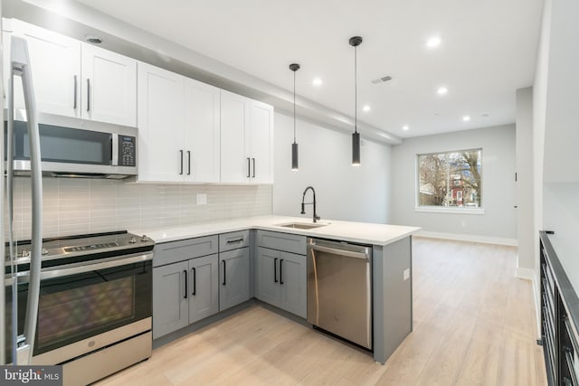 kitchen featuring stainless steel appliances, tasteful backsplash, gray cabinets, light wood-style floors, and a sink