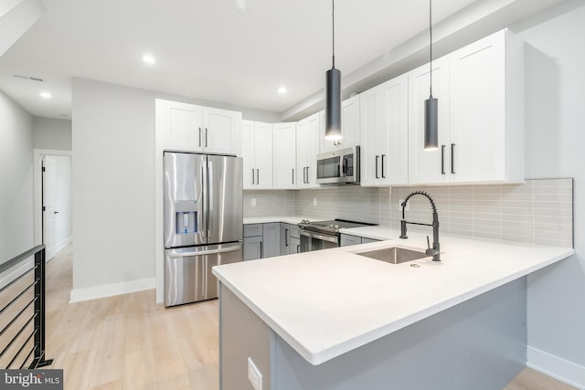 kitchen with light wood finished floors, decorative backsplash, appliances with stainless steel finishes, a peninsula, and a sink