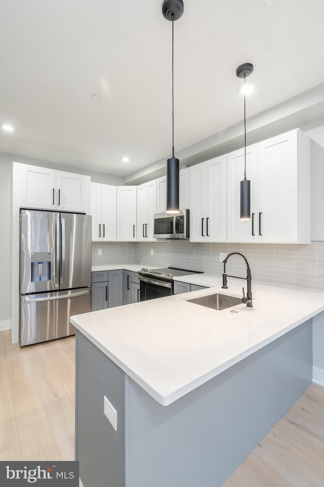 kitchen with stainless steel appliances, light countertops, light wood-style flooring, and a peninsula