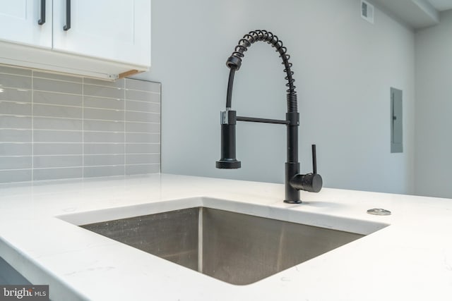 room details with a sink, visible vents, white cabinets, backsplash, and light stone countertops