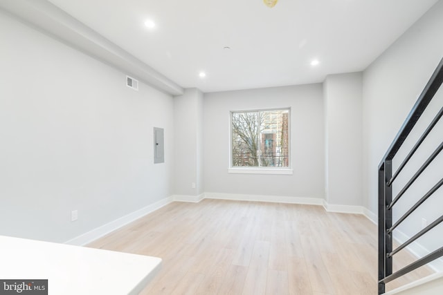 empty room featuring baseboards, light wood-style flooring, visible vents, and electric panel