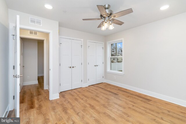 unfurnished bedroom featuring ceiling fan, multiple closets, and light wood-type flooring