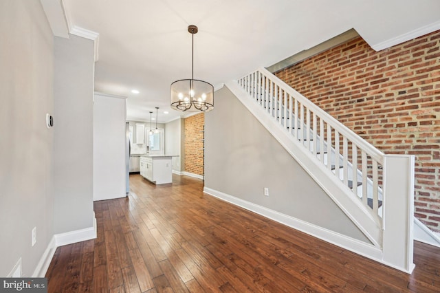 unfurnished living room featuring an inviting chandelier, crown molding, wood-type flooring, and brick wall