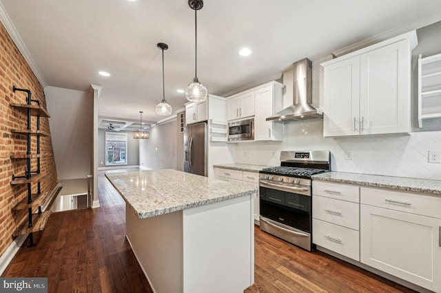 kitchen featuring decorative light fixtures, a center island, wall chimney range hood, stainless steel appliances, and white cabinets