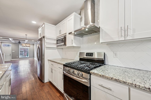 kitchen featuring tasteful backsplash, white cabinets, hanging light fixtures, stainless steel appliances, and wall chimney exhaust hood