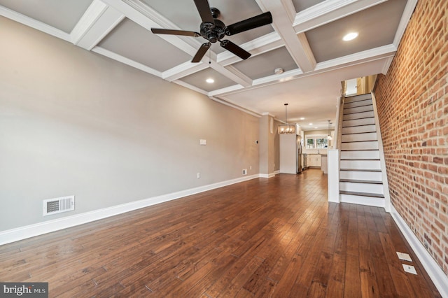 unfurnished living room with brick wall, dark hardwood / wood-style floors, ceiling fan with notable chandelier, coffered ceiling, and crown molding