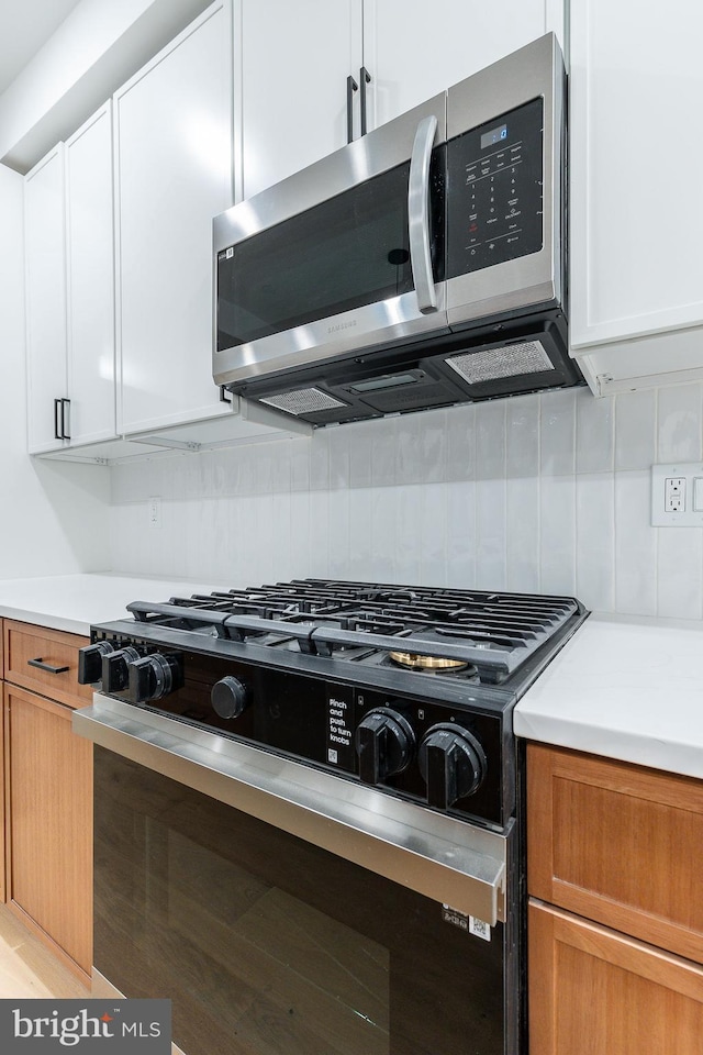 kitchen featuring gas stove, white cabinets, and decorative backsplash