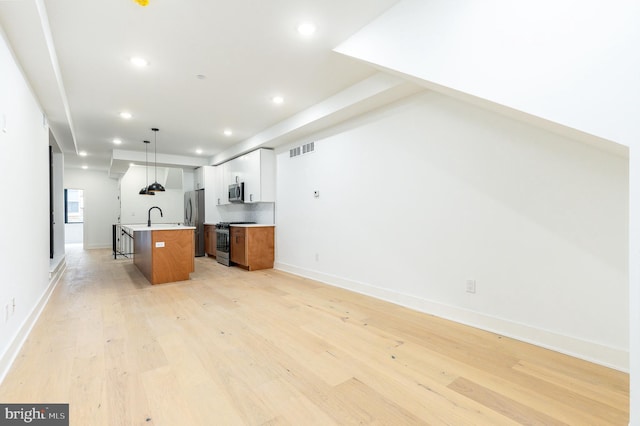 kitchen featuring sink, appliances with stainless steel finishes, white cabinets, a center island with sink, and decorative light fixtures