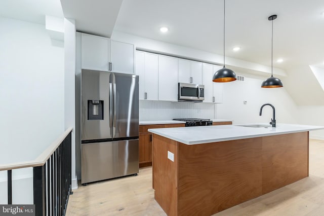 kitchen with appliances with stainless steel finishes, an island with sink, sink, white cabinets, and hanging light fixtures