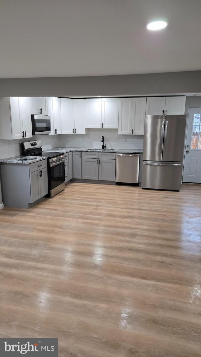 kitchen featuring appliances with stainless steel finishes, sink, light wood-type flooring, white cabinets, and decorative backsplash