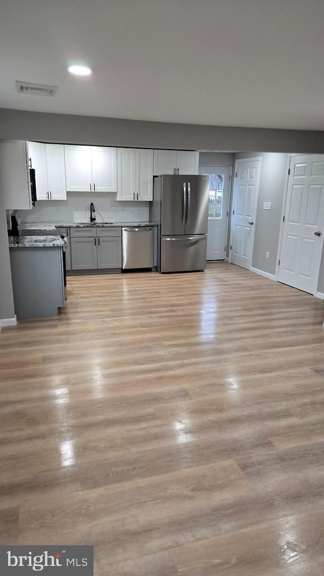 kitchen with stainless steel appliances, stone countertops, sink, and light wood-type flooring