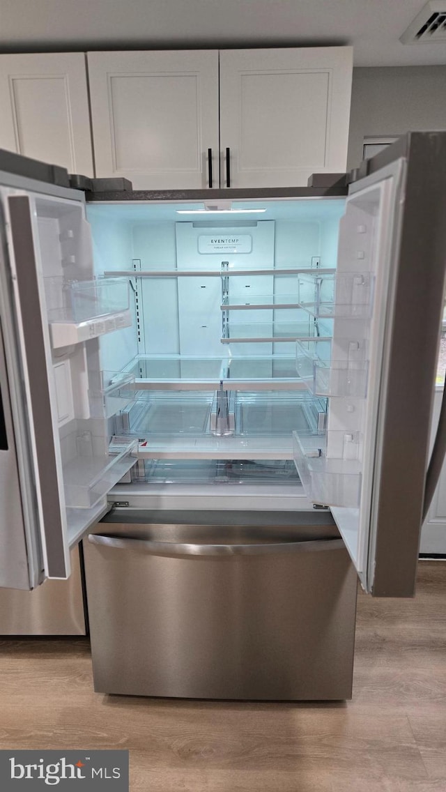 room details with light hardwood / wood-style floors, stainless steel refrigerator, and white cabinets