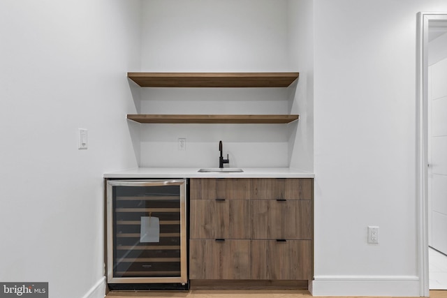 bar featuring baseboards, beverage cooler, light wood-style flooring, wet bar, and a sink