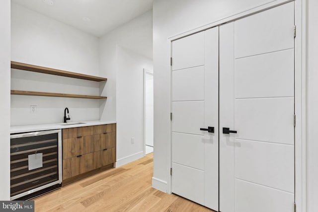 bar featuring beverage cooler, a sink, light wood-style floors, indoor wet bar, and baseboards