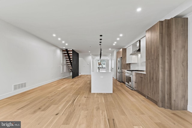 kitchen featuring a center island with sink, visible vents, stainless steel appliances, wall chimney exhaust hood, and modern cabinets