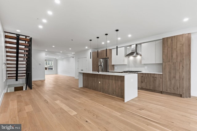 kitchen with wall chimney range hood, light wood-type flooring, appliances with stainless steel finishes, a large island, and modern cabinets