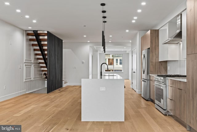 kitchen with modern cabinets, an island with sink, a sink, stainless steel appliances, and wall chimney range hood