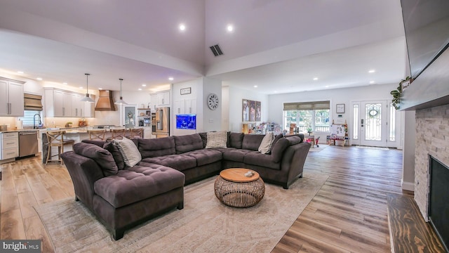 living room featuring sink, a fireplace, a high ceiling, and light wood-type flooring