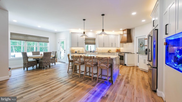 kitchen featuring white cabinets, hanging light fixtures, high end appliances, a center island, and custom range hood