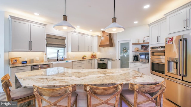 kitchen with pendant lighting, appliances with stainless steel finishes, a kitchen bar, and wall chimney range hood