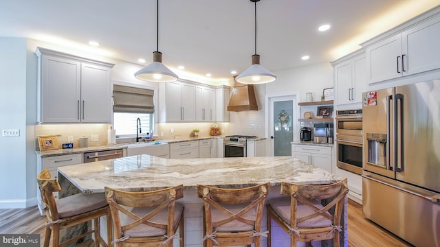 kitchen featuring pendant lighting, custom exhaust hood, stainless steel appliances, and a kitchen island