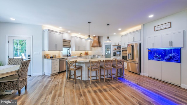 kitchen with premium range hood, hanging light fixtures, appliances with stainless steel finishes, a kitchen island, and white cabinets