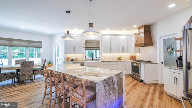 kitchen featuring stainless steel appliances, premium range hood, pendant lighting, and white cabinetry