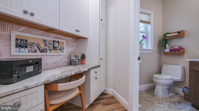 interior space featuring light stone counters, built in desk, light hardwood / wood-style floors, and white cabinets