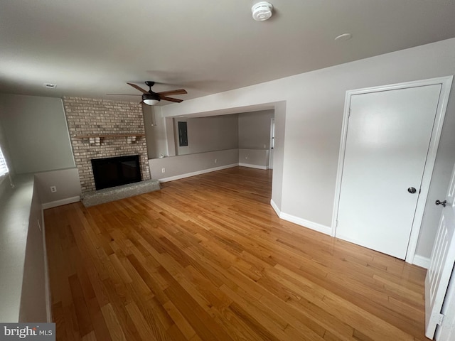 unfurnished living room with ceiling fan, a brick fireplace, and light hardwood / wood-style floors